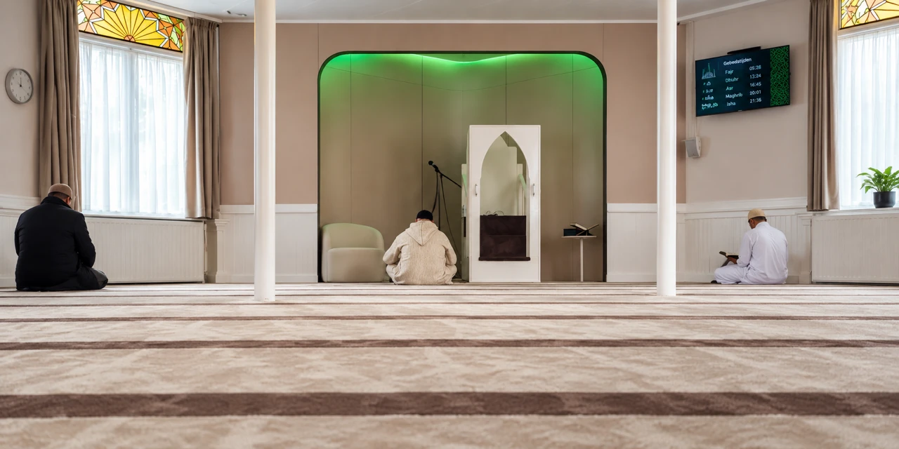 De gebedsruimte van Ittihad Islami: een lichte zaal met tapijt, de mihrab met groen licht en het scherm met gebedstijden aan de muur
